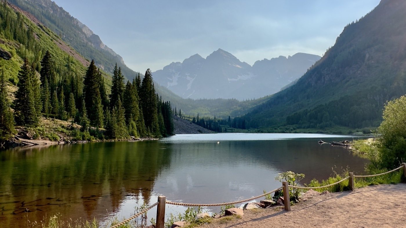 The Maroon Bells rising beyond Maroon Lake, with pine slopes on both sides of the valley.